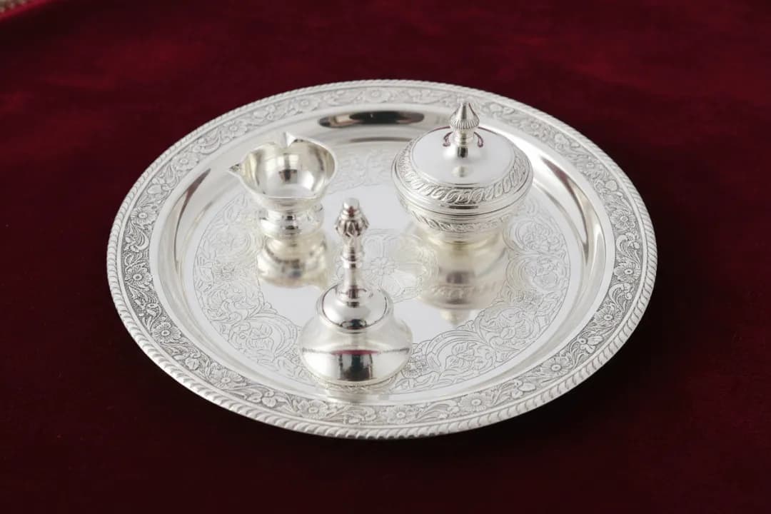Engraved silver pooja thali with katori, ghanti and panchpatra on red velvet